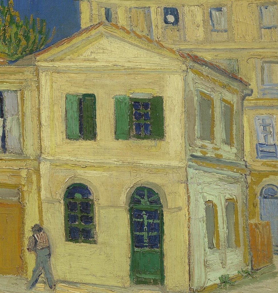 Detalle de La casa amarilla: fachada amarilla con dos ventanas de contraventanas verdes en el primer piso, una casi cerrada y otra abierta, y en la planta baja una ventana y una puerta verdes en arco